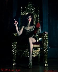 Maîtresse Kym fumant une cigarette en vous regardant dans son trône.